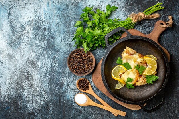 Top view fried fish in pan with lemon and parsley spices in wooden spoons p