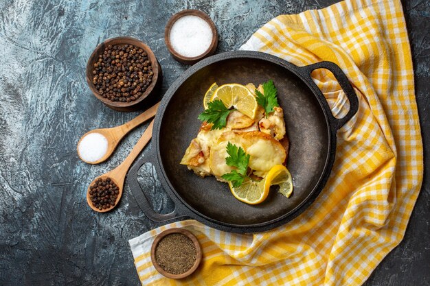 Top view fried fish in pan with lemon and parsley on yellow white checkered tablecloth