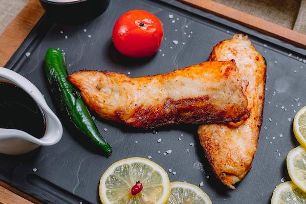 Top view fried fish with vegetables and slices of lemon and pomegranate sauce