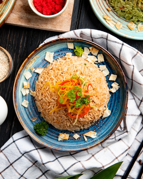 Top view of fried japanese rice with vegetables in soy sauce on a plate on wooden surface