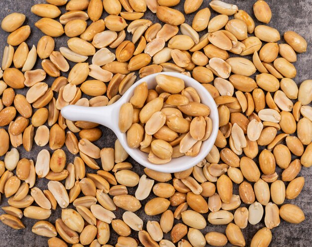 Top view fried peanuts in bowl surrounded by peanuts on stone 