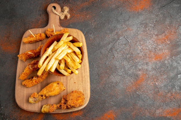 Top view of fried potato and chicken on wooden cutting board