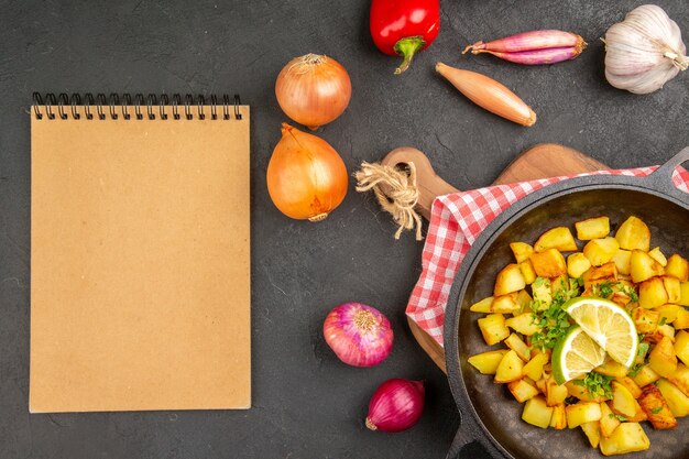 Top view fried potatoes inside pan with fresh vegetables on dark background