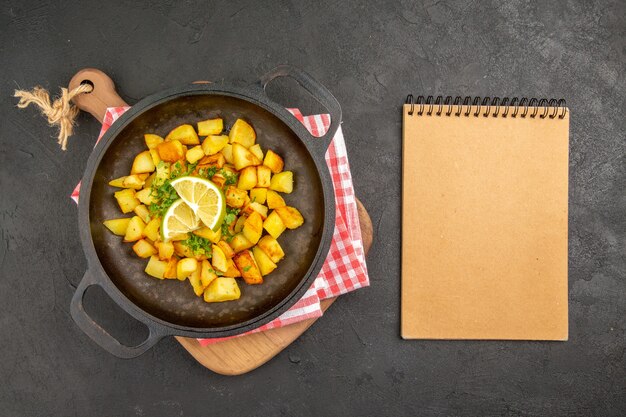 Бесплатное фото Вид сверху жареный картофель внутри сковороды с зеленью и лимоном на темном столе