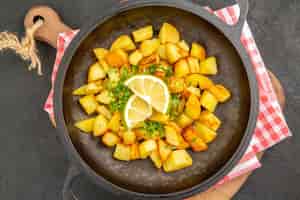 Бесплатное фото Вид сверху жареный картофель внутри сковороды с зеленью и лимоном на темном фоне