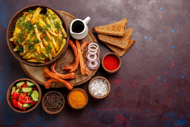 Вид сверху жареный картофель с приправами, буханки хлеба и разные овощи на темном столе