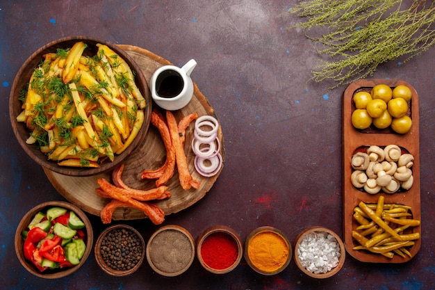 Вид сверху жареный картофель с приправами и разными овощами на темном столе