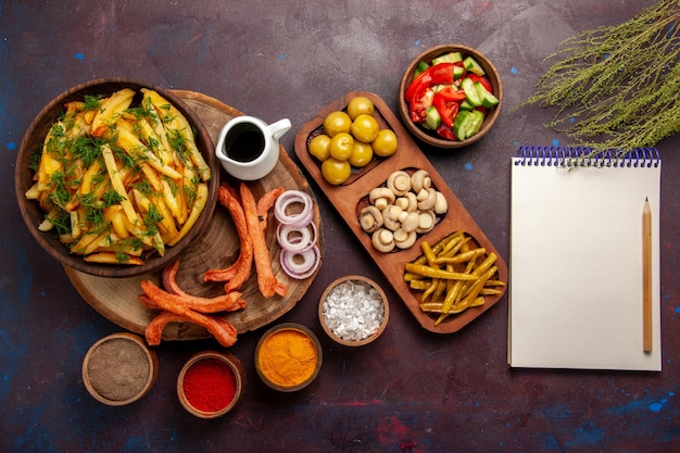 Top view fried potatoes with seasonings and different vegetables on dark surface