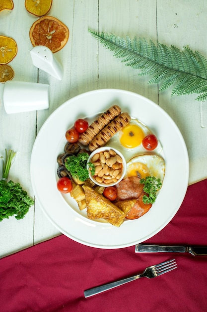 Вид сверху жареной колбасы и яиц с грибами помидорами черри и лобия на белой тарелке