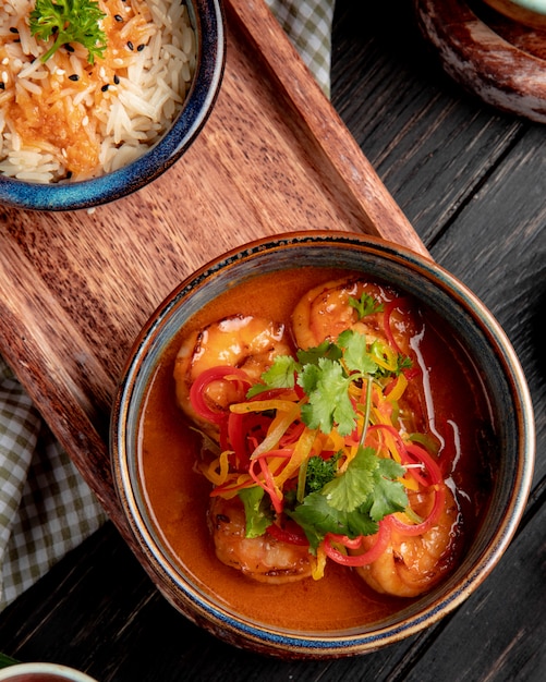 Top view of fried shrimps with vegetables and spicy sauce in a bowl on wood board on rustic