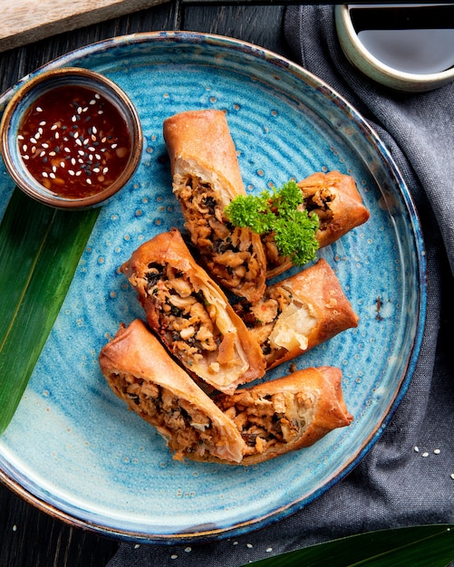 Top view of fried spring rolls with chicken and vegetables served with soy sauce on a plate on black