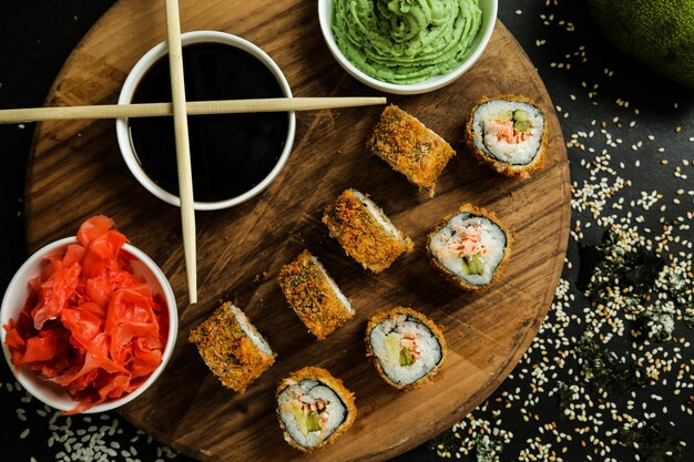 Top view fried sushi rolls on a stand with ginger soy sauce and wasabi with chopsticks