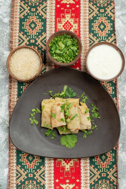 Top view from afar appetizing dish appetizing plate of stuffed cabbage herbs rice sour cream on colored tablecloth with patterns in the center of grey table