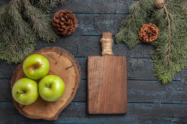 Top view from afar apples board cones three green apples on cutting board and wooden kitchen board between tree branches with cones