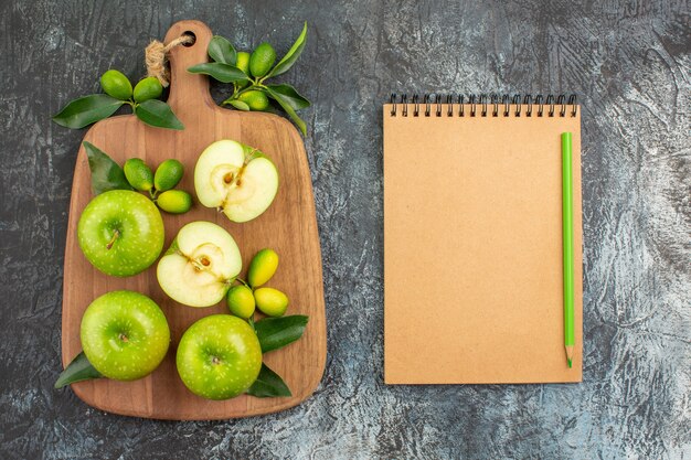 Top view from afar apples green apples citrus fruits on the board cream notebook and pencil