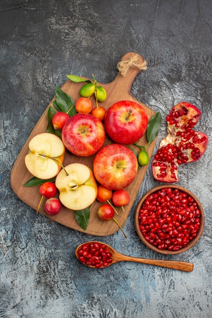 Top view from afar apples pomegranate in the bowl apples cherries on the cutting board