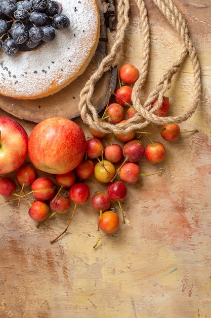 Top view from afar a cake a cake on the wooden board the appetizing apples berries rope