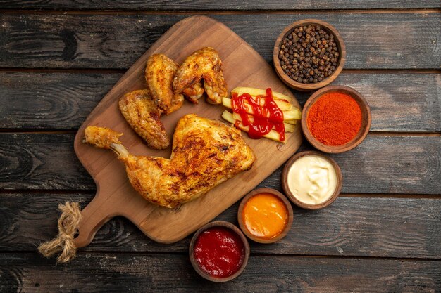 Top view from afar chicken bowls of spices and sauces next to the chicken with french fries and ketchup on the cutting board