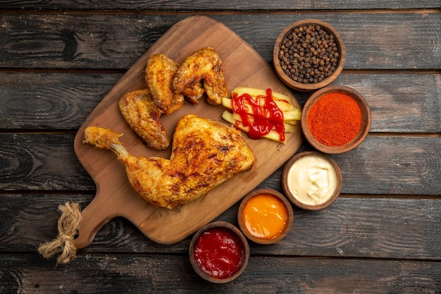 まな板の上にフライドポテトとケチャップを添えた鶏肉の横にあるスパイスとソースの遠くの鶏肉ボウルからの上面図