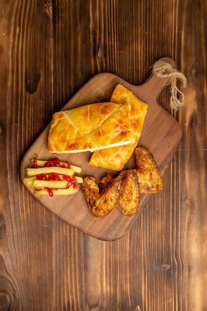 Vista dall'alto da lontano pollo e torta ali di pollo torta e patatine fritte con ketchup sul tagliere