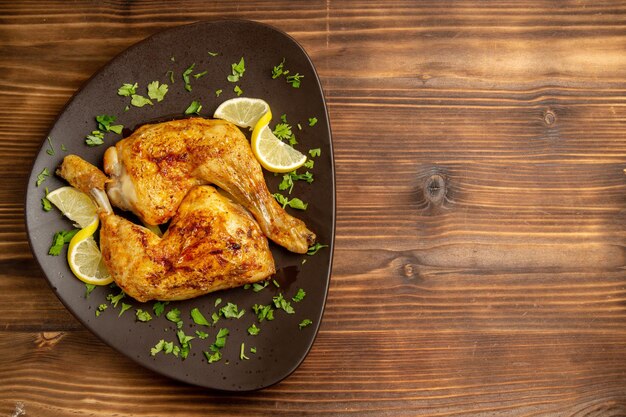 테이블 왼쪽에 있는 접시에 허브와 레몬을 넣은 레몬 닭 다리가 있는 멀리 있는 닭의 꼭대기