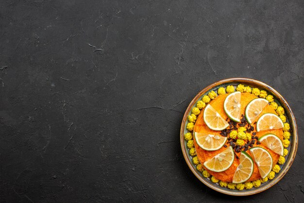 Top view from afar citrus fruits and chocolate appetizing cake with chocolate and citrus fruits on the right side of the black table