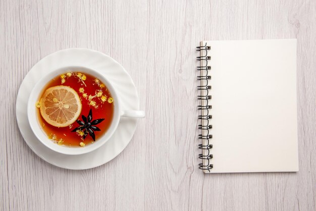 Top view from afar a cup of tea on the saucer a cup of tea with lemon on the saucer next to the white notebook on the light table