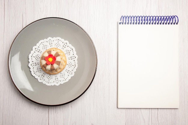 Вид сверху издалека кекс кекс на белой кружевной салфетке на тарелке рядом с белой записной книжкой на столе