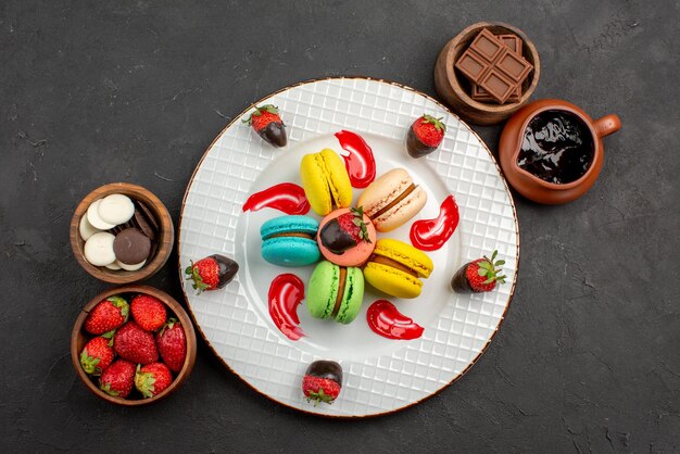 Top view from afar dessert plate of French macaroons and strawberries between bowls of chocolate strawberries and chocolate cream on the table
