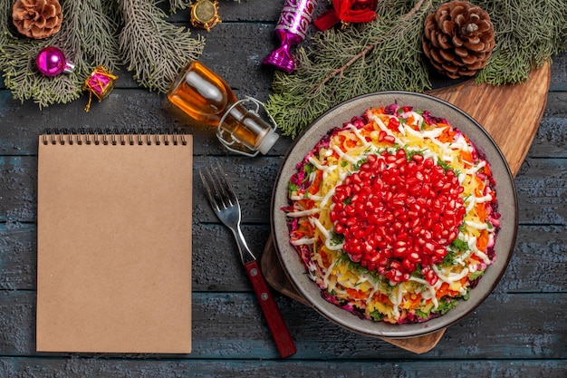오일 포크 크림 공책 옆 도마에 석류가 있는 접시 접시에 있는 멀리 있는 접시와 콘과 크리스마스 트리 장난감이 있는 나뭇가지