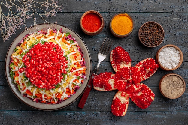 Free photo top view from afar dish of pomegranate dish of pomegranate next to the peeled pomegranate fork and bowls of different spices