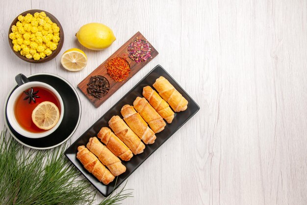 Top view from afar dish on the wooden tale with tree branches next to the black cup of tea with lemon bowls of sweets and spices lemon next to the plate of tubular pastry on the table