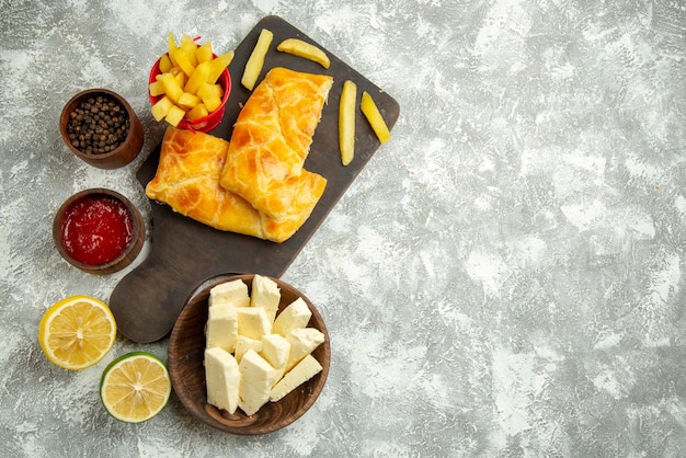 無料写真 灰色のテーブルの上のチーズケチャップと黒胡椒レモンのボウルの横にあるボード上の遠くのファーストフード2つのパイとフライドポテトからの上面図