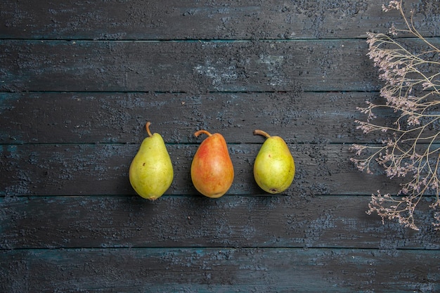 Top view from afar green-yellow-red pears two green pears and one red-yellow pear in the center of grey table next to the tree branches