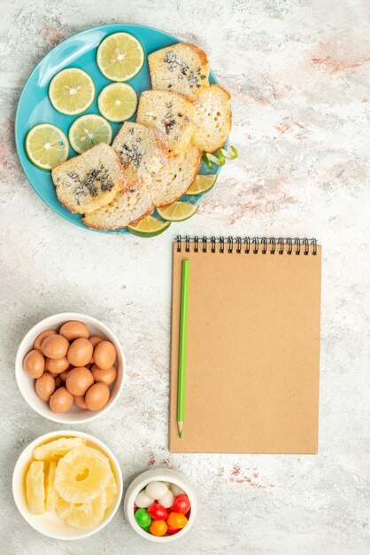 Top view from afar lemon bread white bread with herbs lemon in the plate next to notebook pencil bowls of candies on the table