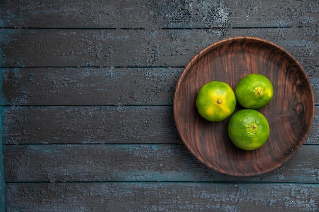 Top view from afar limes in bowl wooden brown bowl of limes on the right side of the grey table