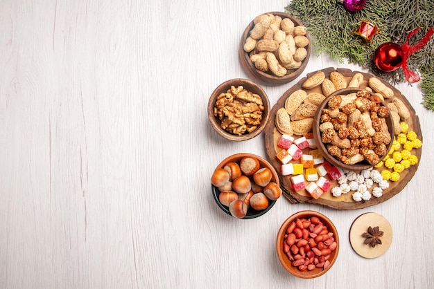 Top view from afar nuts on the board spruce branches with different sweets and peanuts on the kitchen board next to the bowls of hazelnuts walnuts on the table