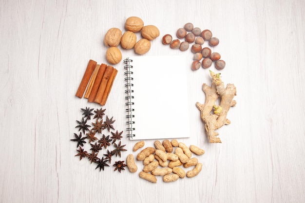 Top view from afar nuts different kinds of nuts and cinnamon sticks around the white notebook on the white table