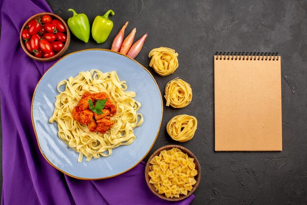 Вид сверху макароны и мясная миска с помидорами, шарик, перец, лук рядом с кремовой пастой для ноутбука и тарелка макарон на фиолетовой скатерти