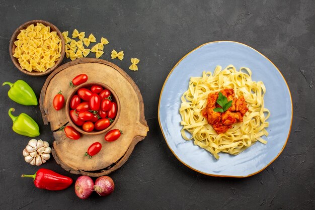 Top view from afar pasta and tomatoes plate of pasta with meat brown bowl of tomatoes on the wooden board pasta and onion bell pepper and garlic on the table