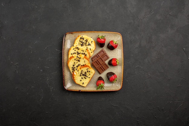 Бесплатное фото Вид сверху на кусочки торта аппетитной клубники в шоколаде и кусочки торта с шоколадом на квадратной тарелке на темном столе