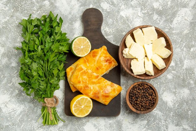 회색 탁자에 있는 검은 후추 치즈와 허브 옆에 있는 나무 판자에 있는 멀리 있는 파이 허브 치즈 파이와 레몬의 꼭대기