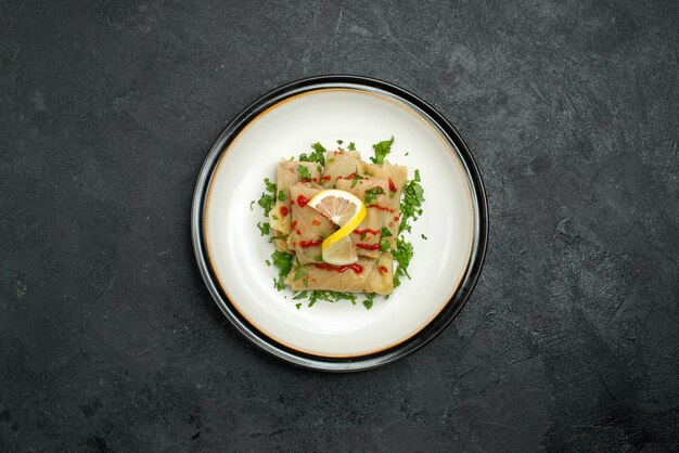 Top view from afar plate of appetizing dish stuffed cabbage with lemon herbs and sauce on a white plate in the center of black table