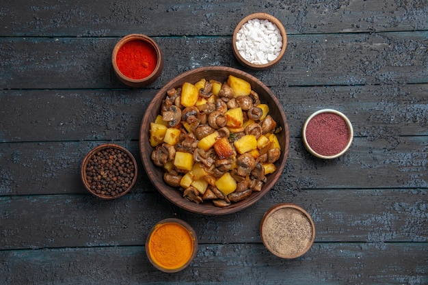 Foto gratuita vista dall'alto da lontano piatto e ciotola di spezie con patate e funghi e spezie colorate intorno a loro