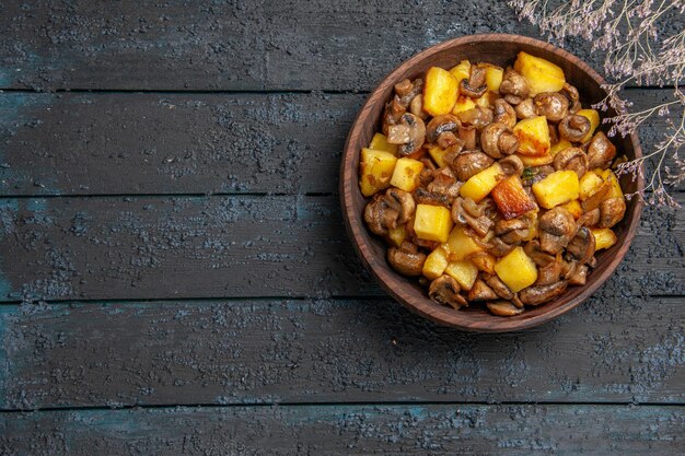 Top view from afar plate with food brown bowl with potatoes and mushrooms next to the branches on the right of the table