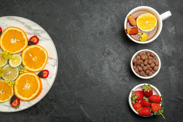 Top view from afar sliced orange plate of sliced orange lemon chocolate-covered strawberries next to the cup of tea hizelnuts and strawberries