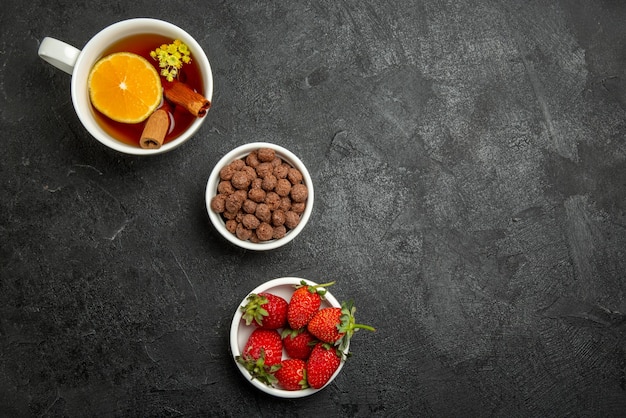 Top view from afar strawberries hizelnuts brown bowls of strawberries hizelnuts and a cup of tea with lemon on the dark table