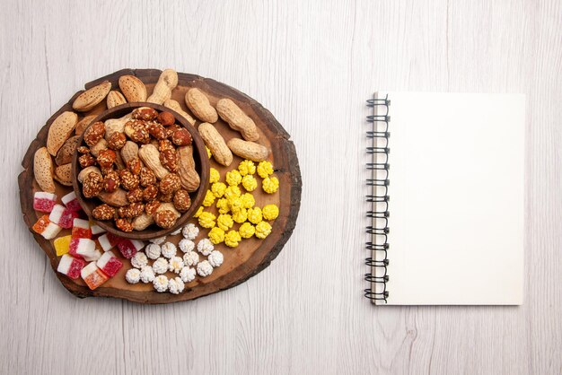 Top view from afar sweets in bowl white notebook next to the cutting board with sweets and bowl of peanuts on the white table