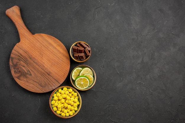 Top view from afar sweets chocolate limes and yellow candies in bowls and the cutting board on the dark background