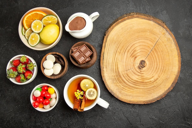 무료 사진 탁자 위에 있는 멀리 있는 과자의 꼭대기에서 계피와 레몬을 넣은 차 한 잔, 나무 판자 옆에 있는 딸기 초콜릿과 사탕 한 그릇